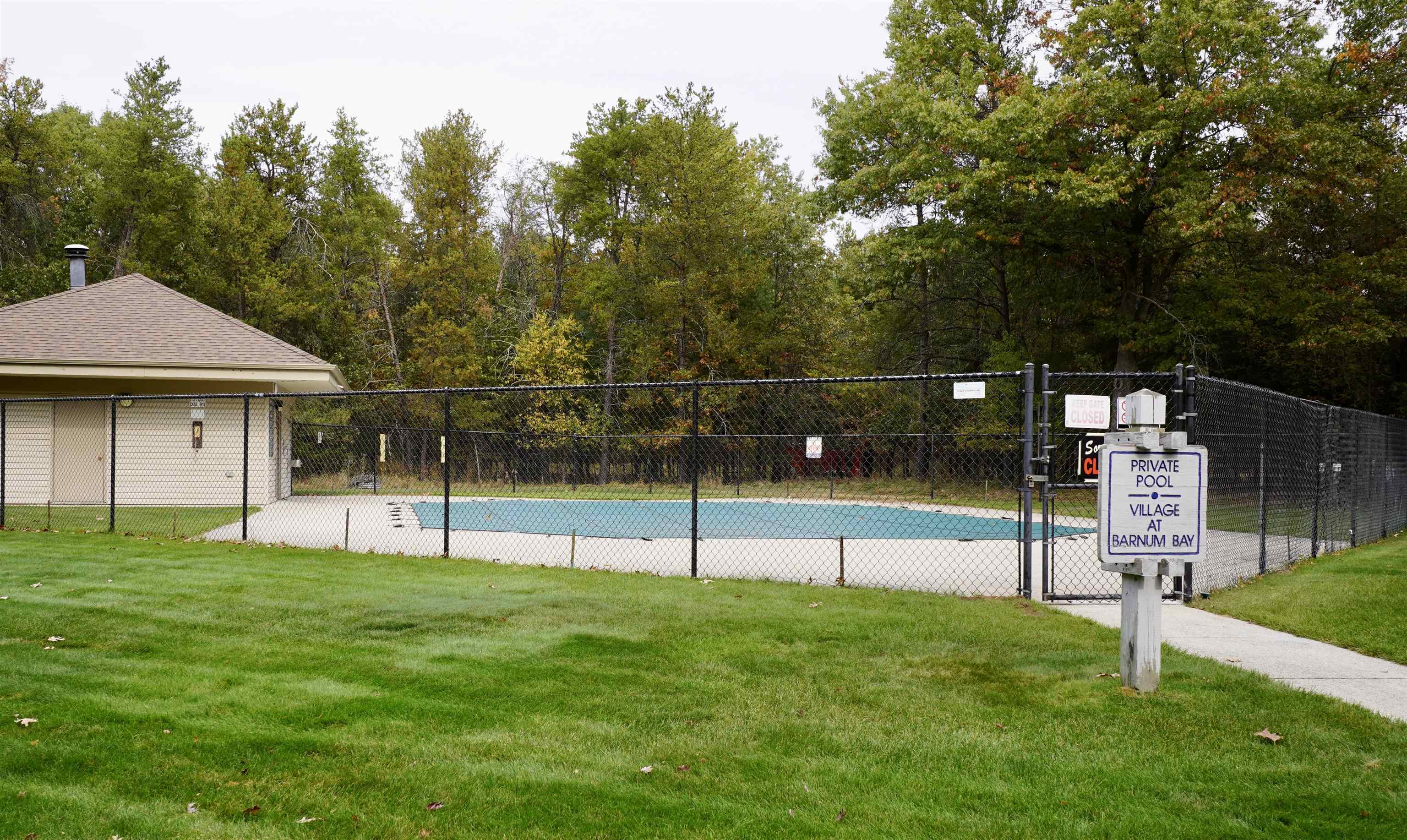 Community pool behind a chain-link fence, with a Village at Barnum Bay private pool sign.