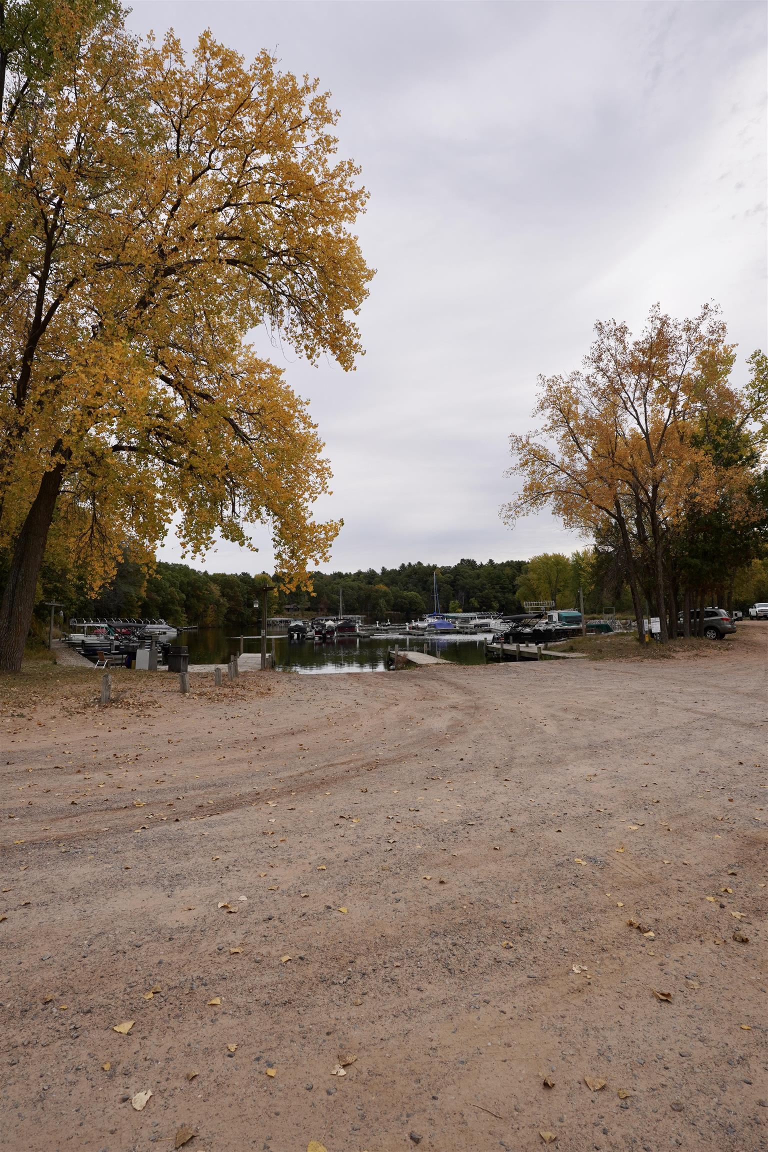 Marina with docked boats framed by autumn trees beside a gravel access area.