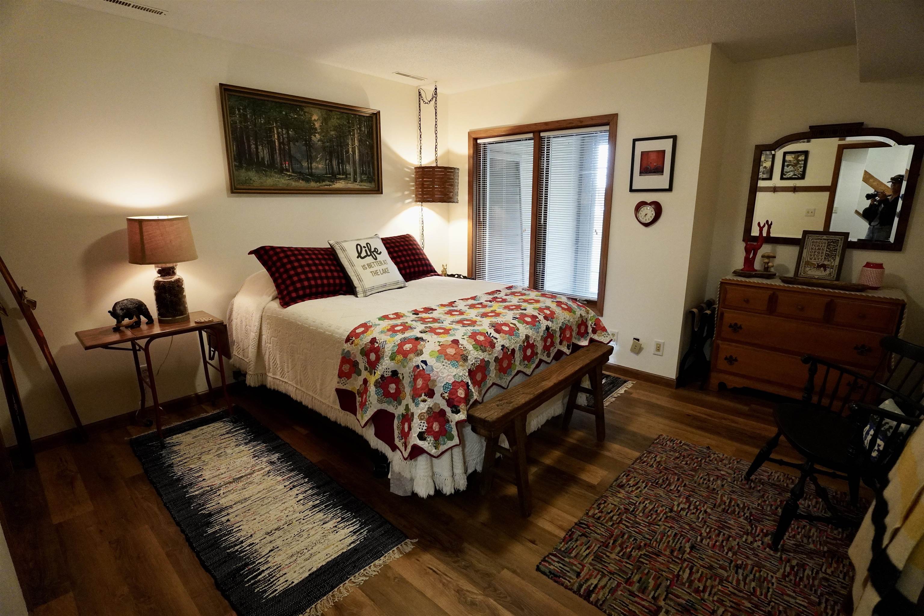 Furnished bedroom with a colorful floral quilt, check pillows, and wood furnishings.