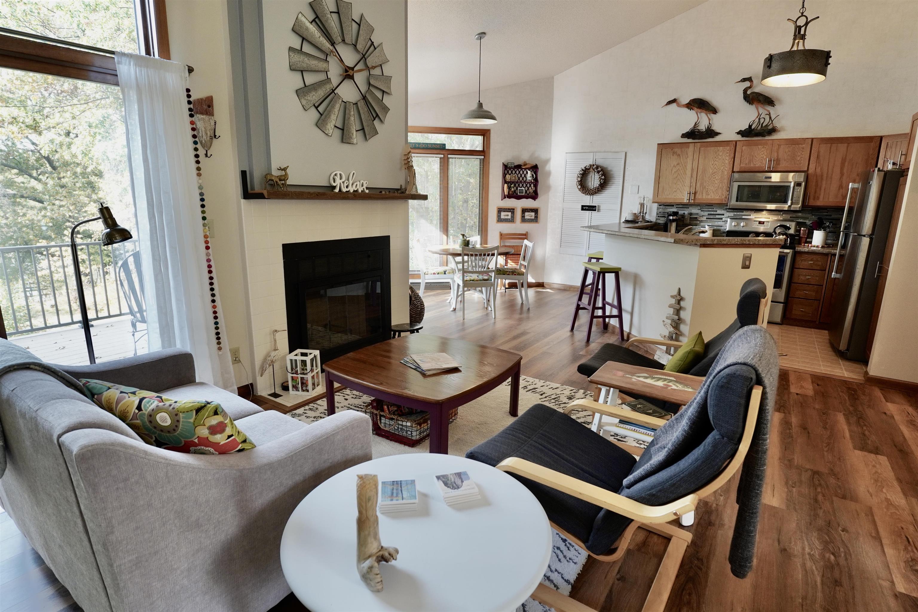 Open-plan living room with a tiled fireplace, balcony windows, and an adjoining kitchen with an island.
