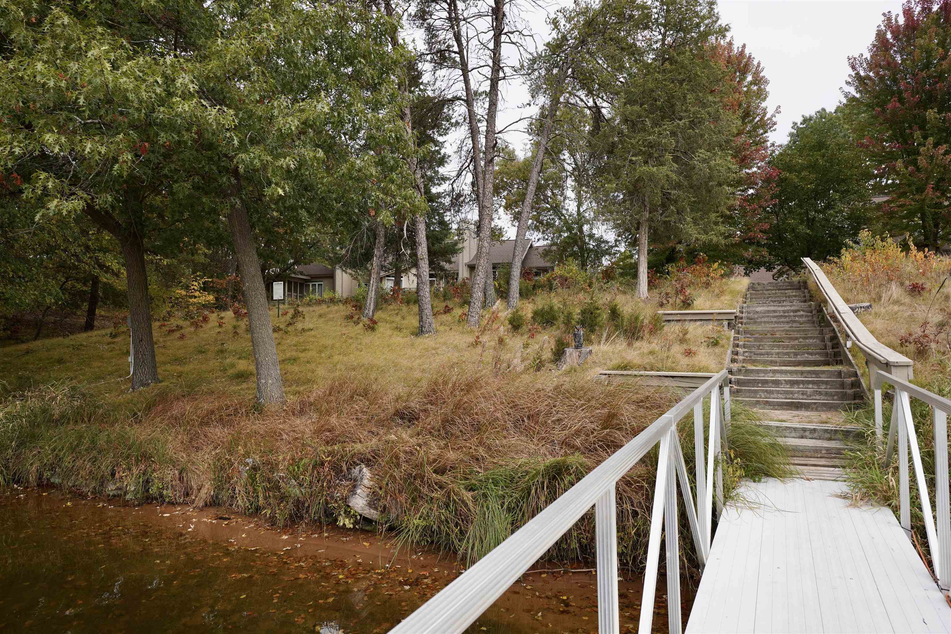 Wooded creekside property with a white-railed walkway and stairs leading toward a partially hidden house.