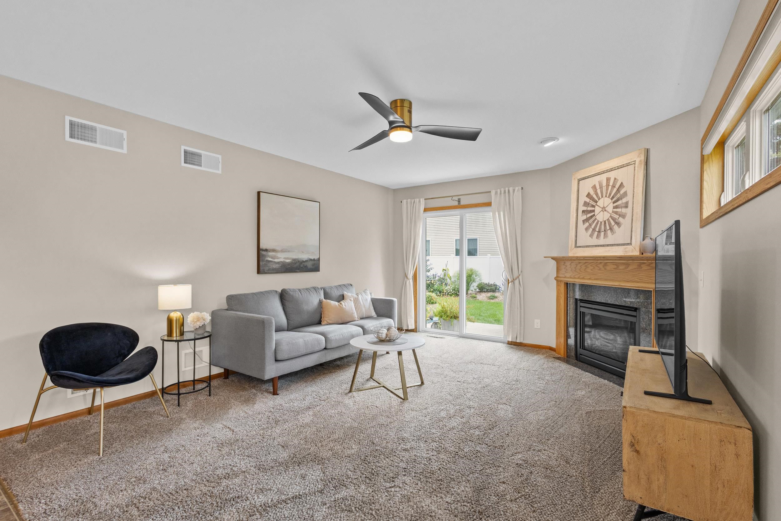 Staged living room with a gray sofa, sliding glass door, and fireplace with a wood mantel.