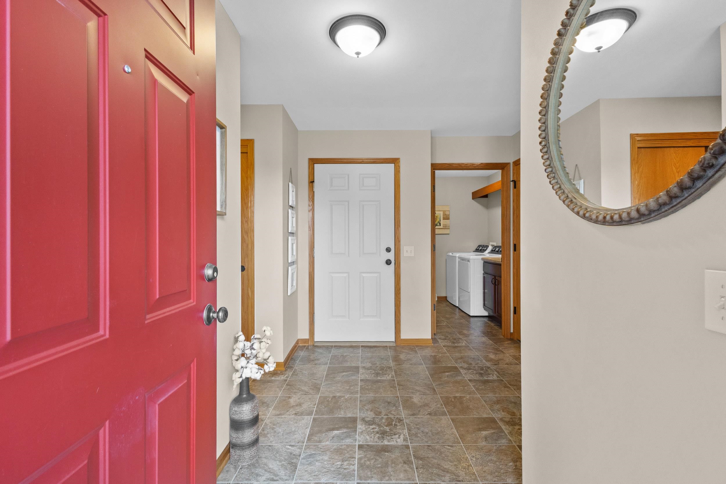 Foyer with tiled floor, red front door, round mirror, and laundry area beyond.