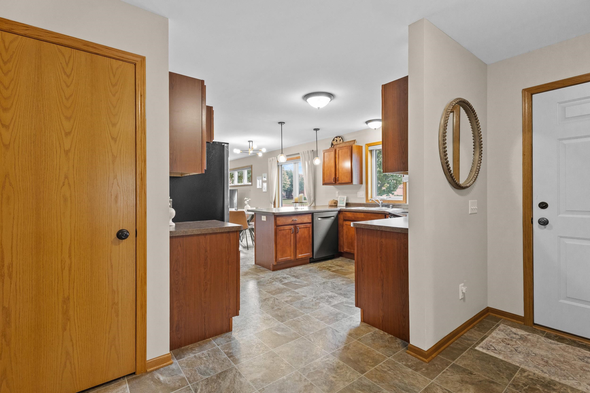 Kitchen with warm wood cabinets and tiled floors, viewed from the entry beside a white door.