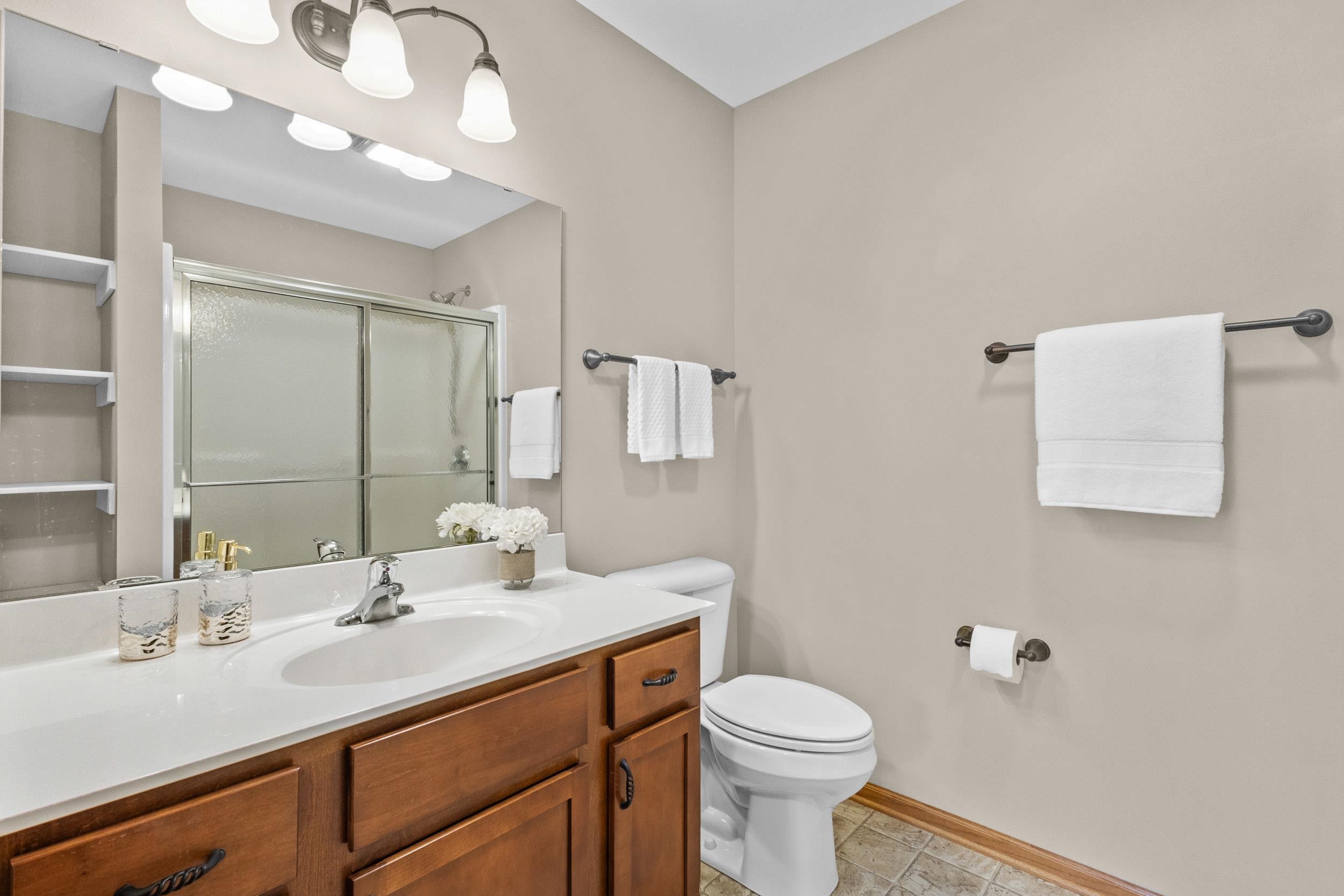 Bathroom with a wood vanity, mirrored shower doors, and white towels.