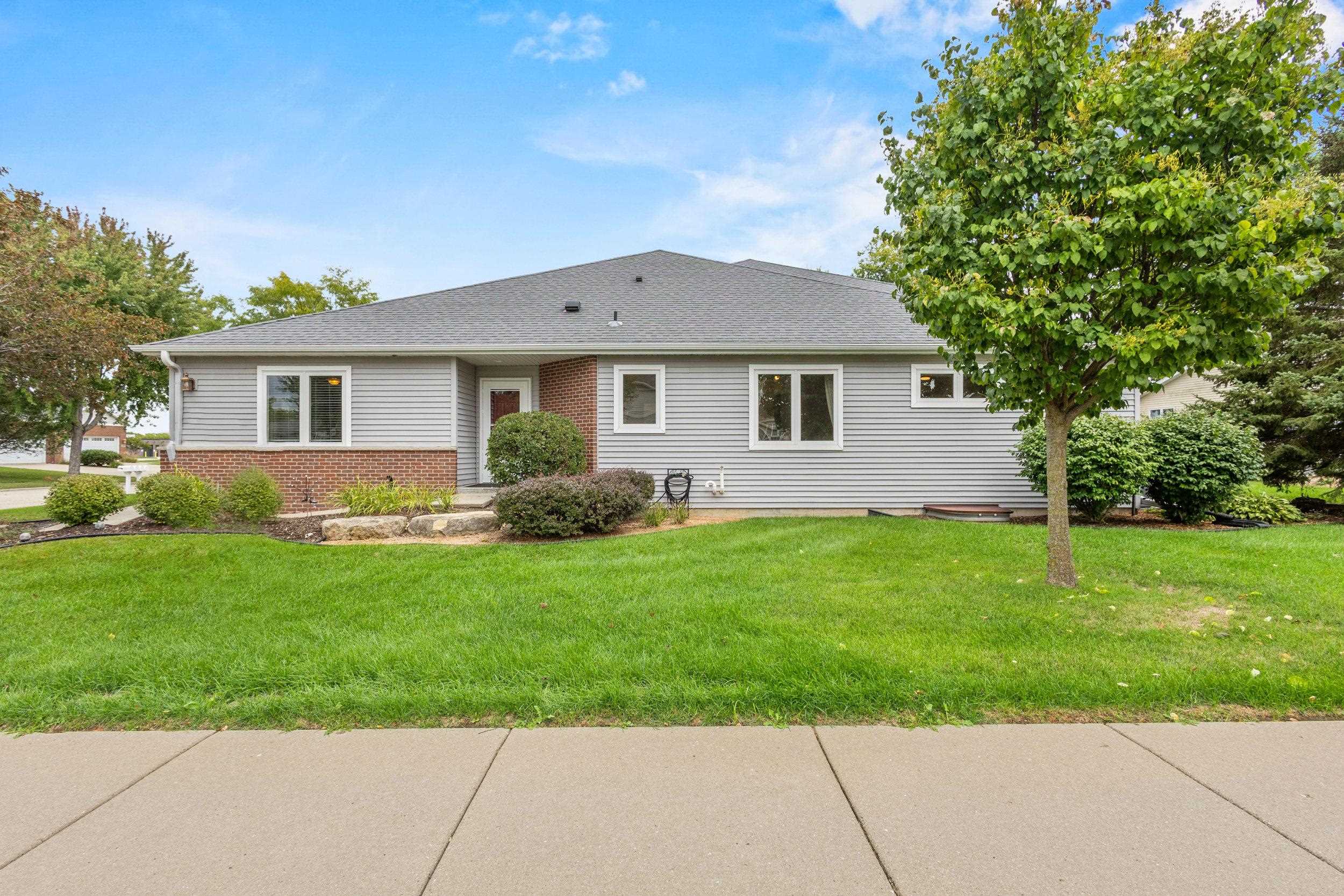 Single-story gray-sided house with brick accents, a broad lawn, and a large tree.