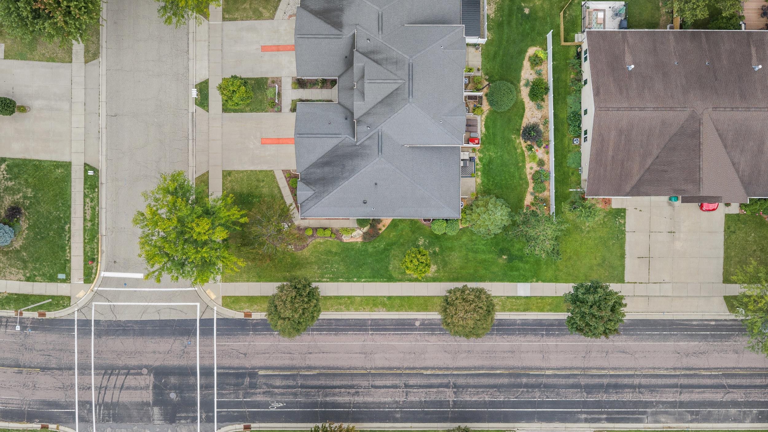 Aerial view of a gray-roofed home, front lawn, and landscaped yard beside the street.