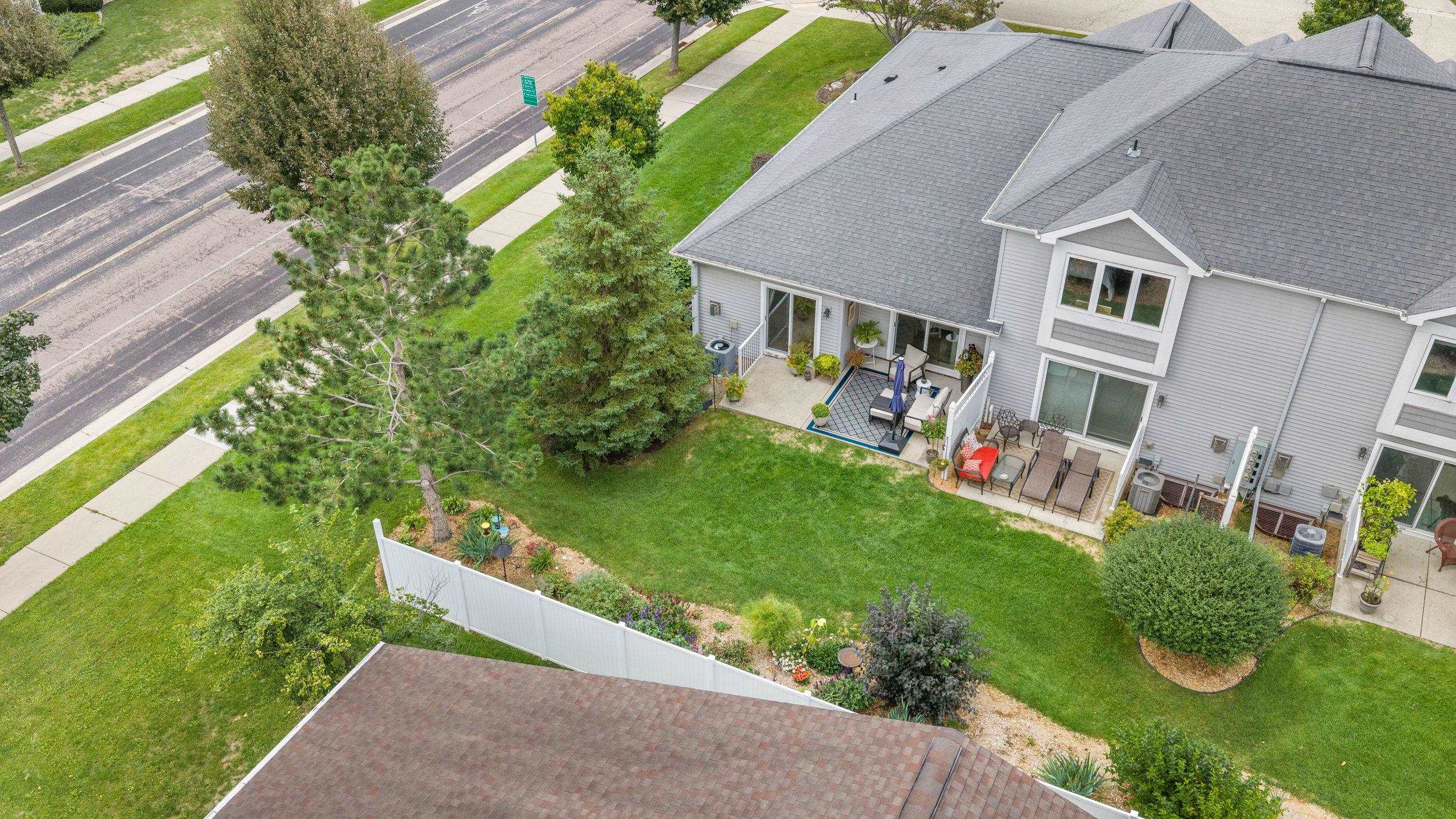 Aerial view of a gray-sided home, furnished patios, and a landscaped fenced lawn.