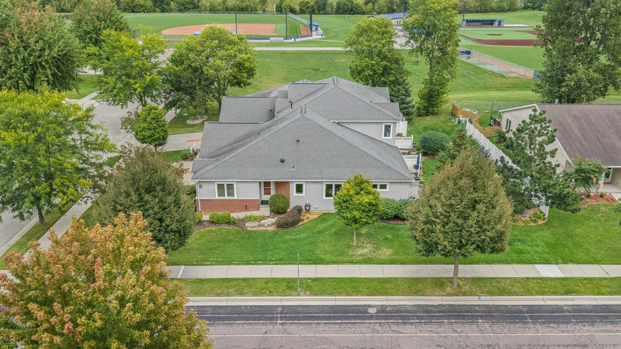 Aerial view of a gray-roofed home with landscaped lawn and baseball fields behind it.