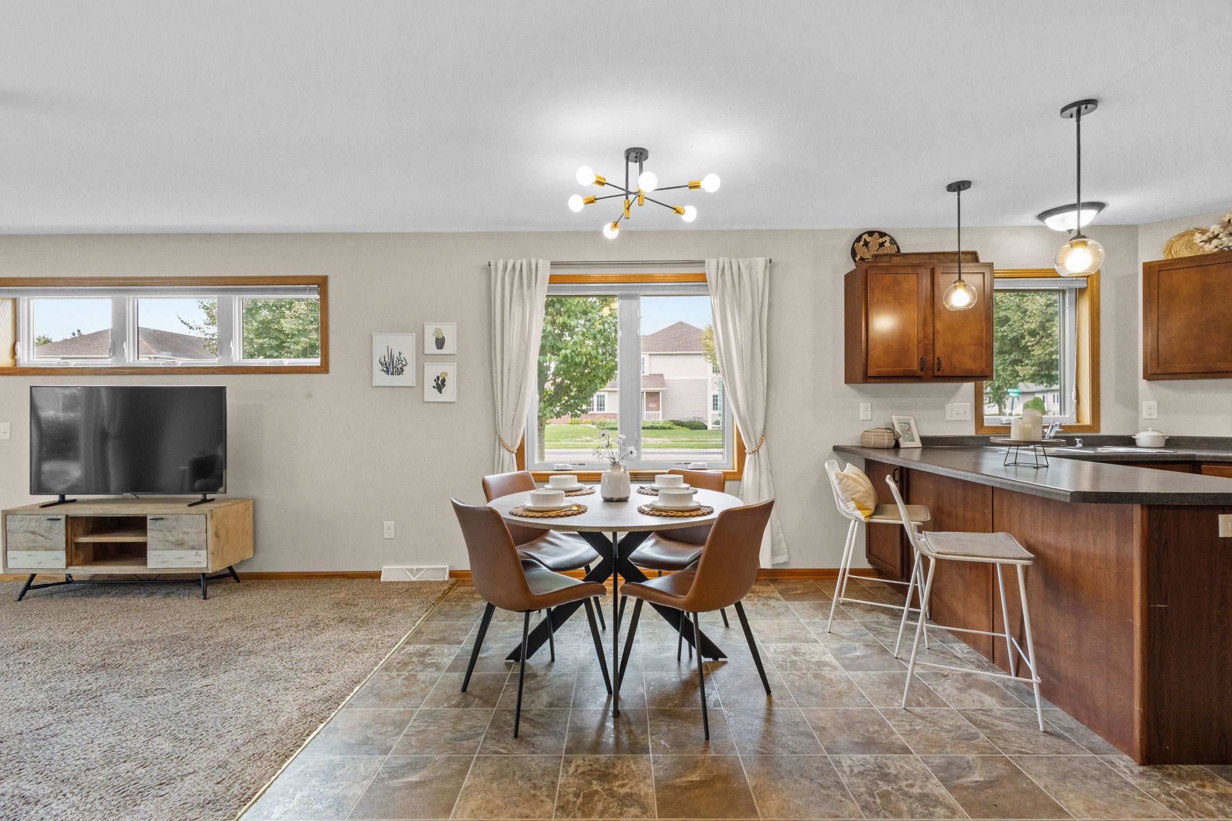 Open-plan kitchen and dining area with dark wood cabinets, breakfast bar, and round table by curtained windows.