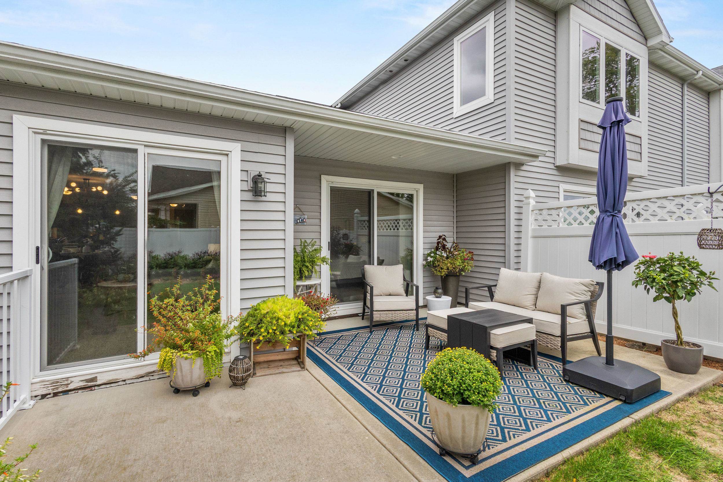 Furnished patio with cushioned seating, potted plants, a blue patterned rug, and a closed purple umbrella.