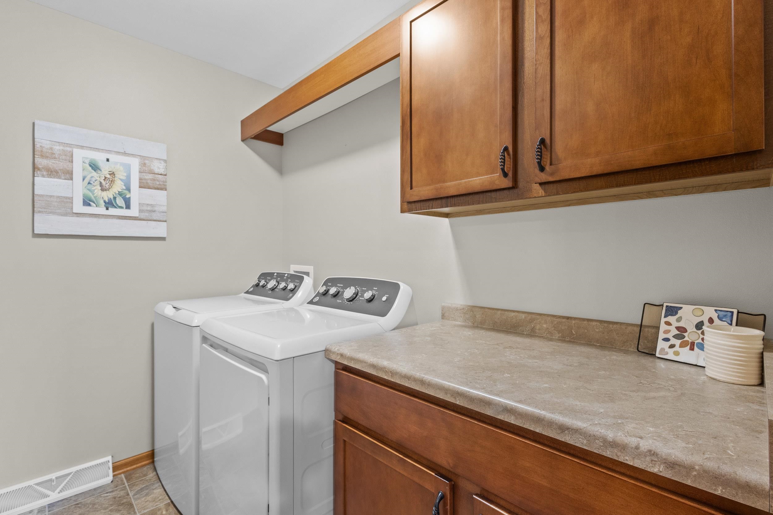 Laundry room with white washer and dryer beneath wood cabinets and a beige countertop.