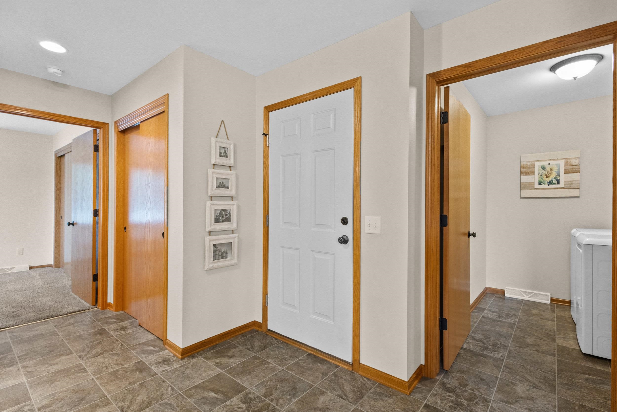 Entryway with a white front door, gray tile floors, wood trim, and a washing machine in the adjacent laundry area.