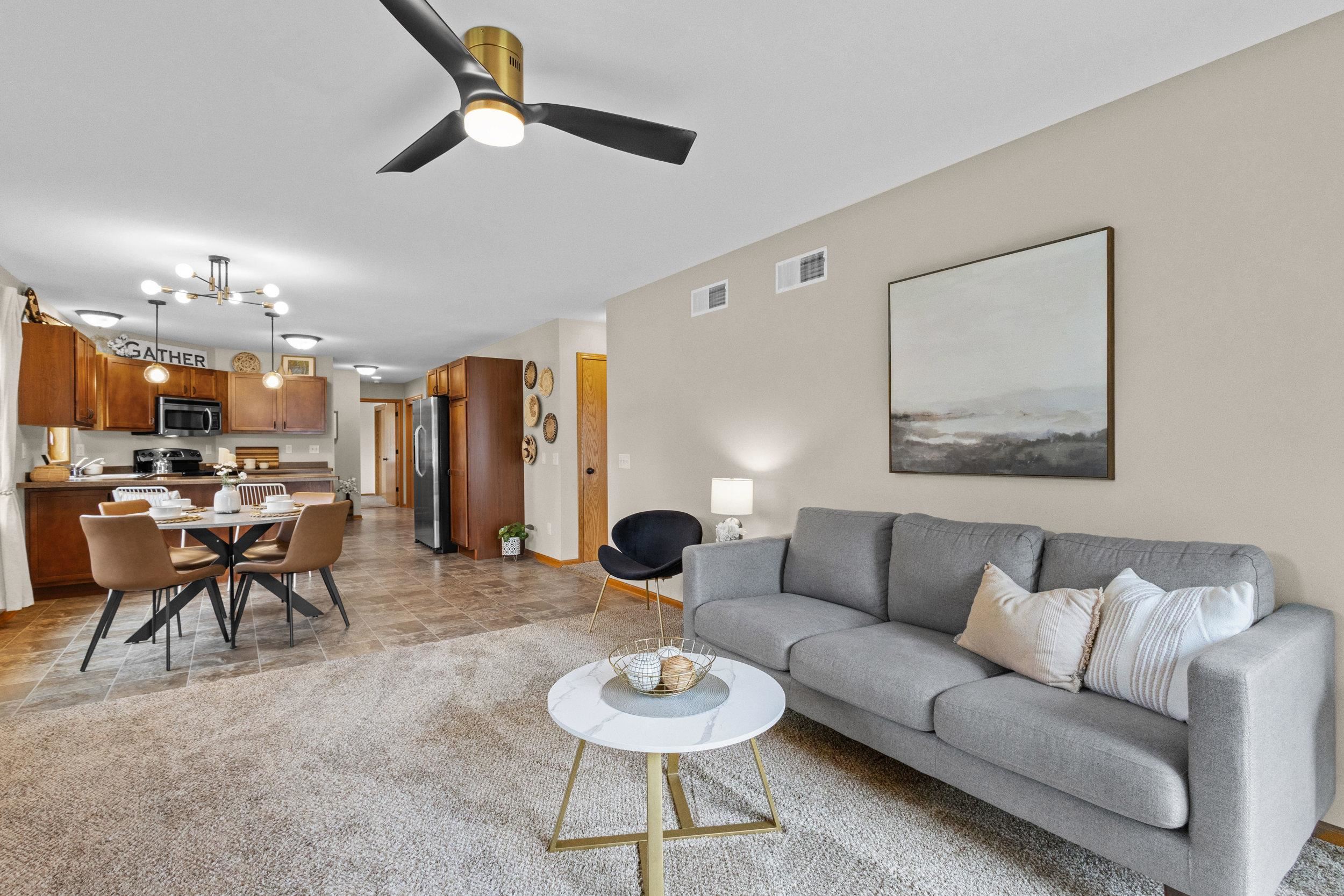 Open-plan living room, dining area, and kitchen with a gray sofa and wood cabinetry.