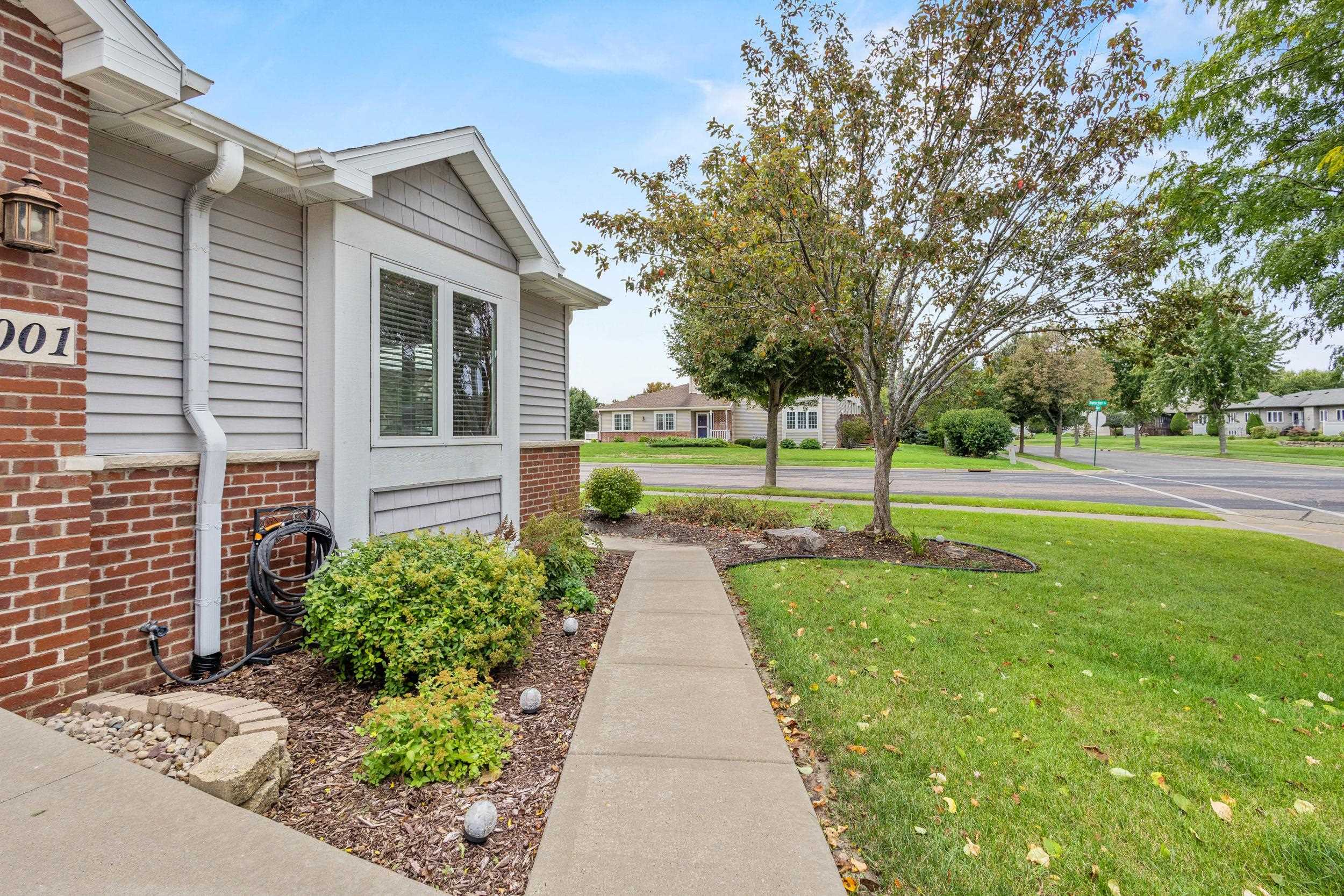 Gray-sided home with brick accents and a landscaped walkway leading toward the street.
