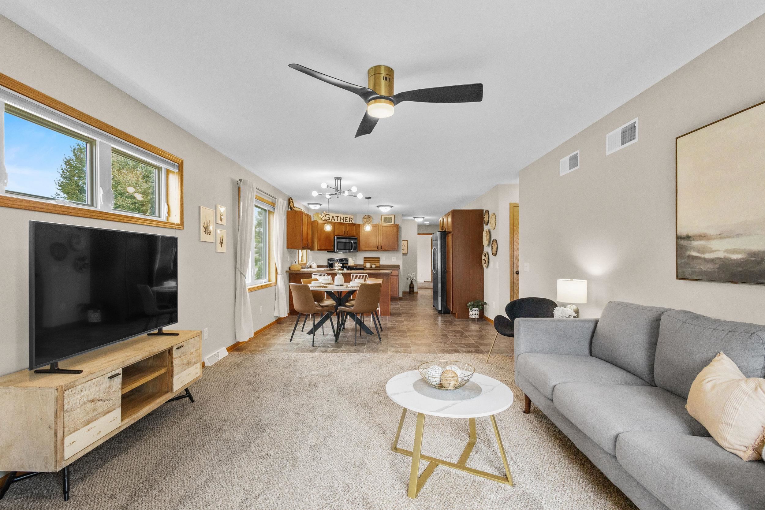 Open-plan living room and kitchen with a gray sofa, dining table, and wood cabinets.