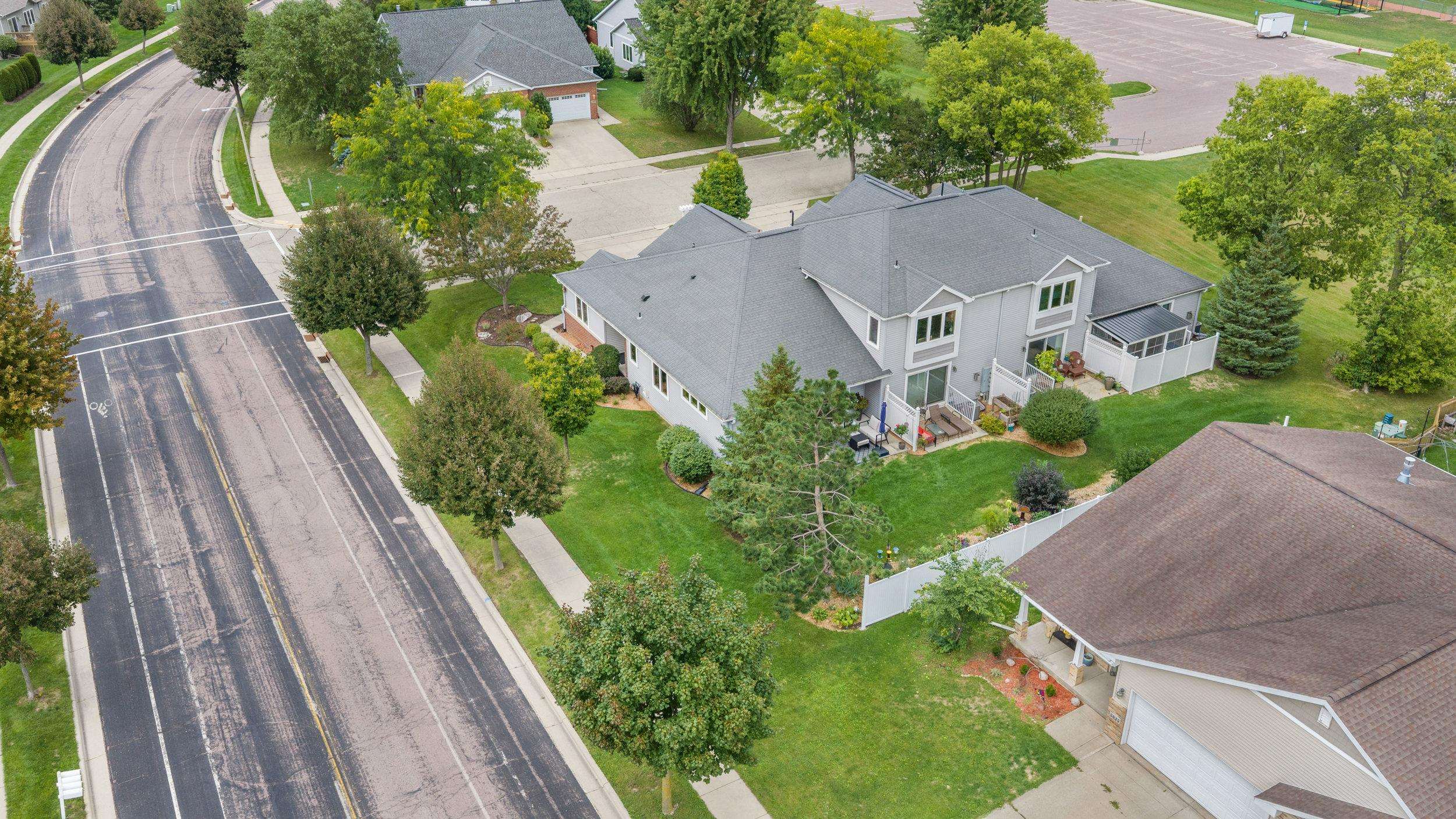 Aerial view of a gray-sided home with two patios, a landscaped yard, and a neighboring street.