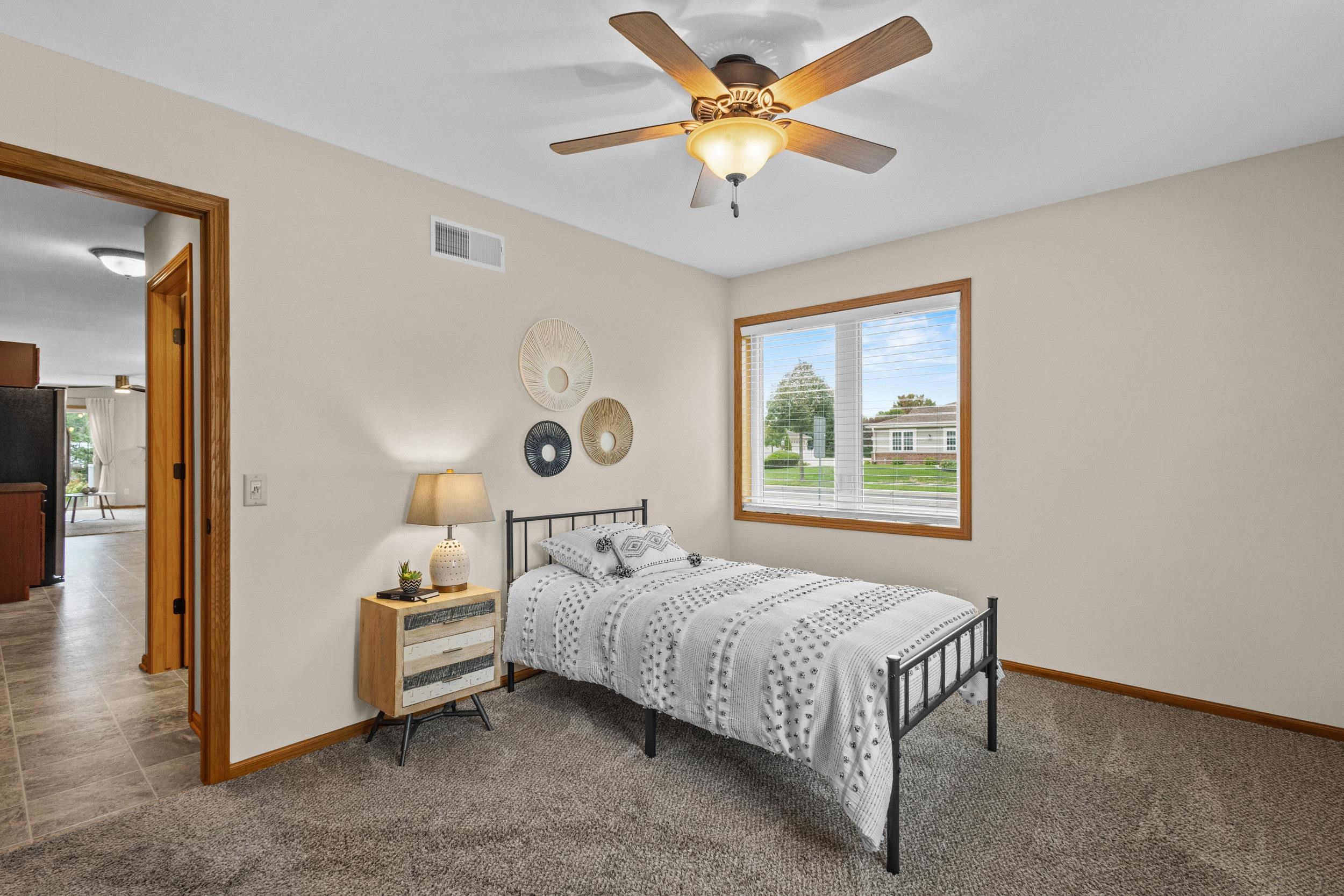 Staged bedroom with patterned white bedding, a wood-trimmed window, and a ceiling fan.
