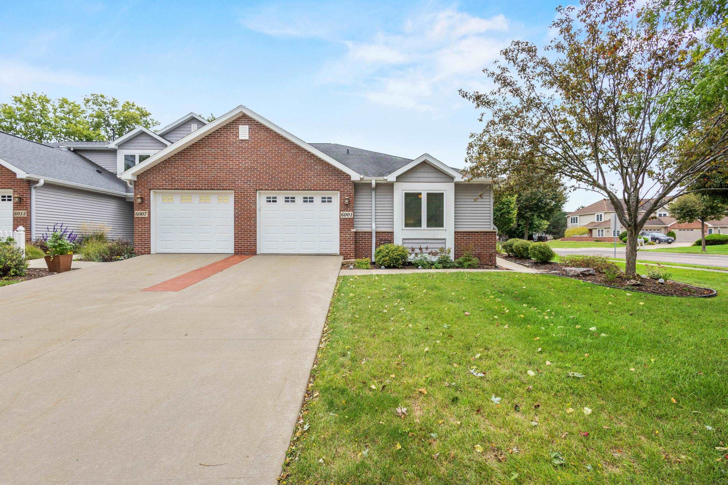 Home with red brick and gray siding, two garage doors, a broad driveway, and a front lawn.