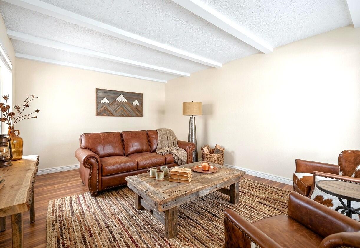 Living room with leather seating, a rustic coffee table, woven rugs, and exposed ceiling beams.