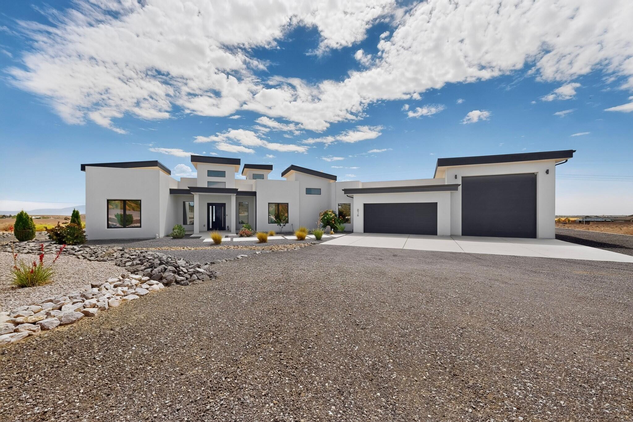 Modern white home with angular rooflines, two dark garage doors, and desert gravel landscaping.