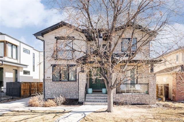 Two-story brick house with a green front door behind a large leafless tree.