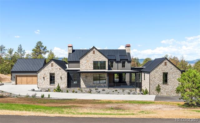 Modern stone house with black metal roofs, a central porch, and attached garage wings.