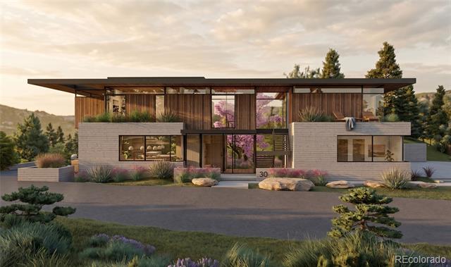 Modern two-story home with a broad flat roof, wood siding, pale masonry, and landscaped grounds.