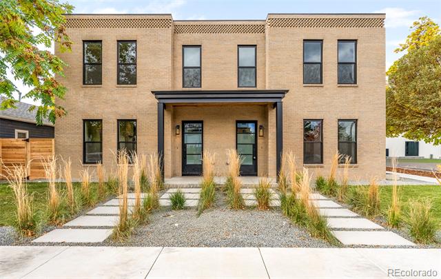 Modern tan brick home with a covered entry and landscaped paths through ornamental grasses.