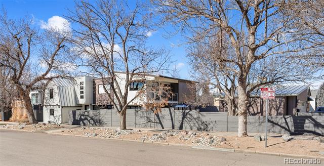 Modern multi-unit homes behind a low fence and leafless trees along a Denver street.