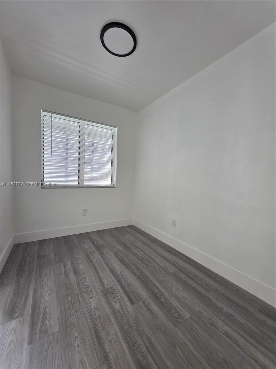 Unfurnished room with gray plank flooring, a window with blinds, and a round ceiling light.
