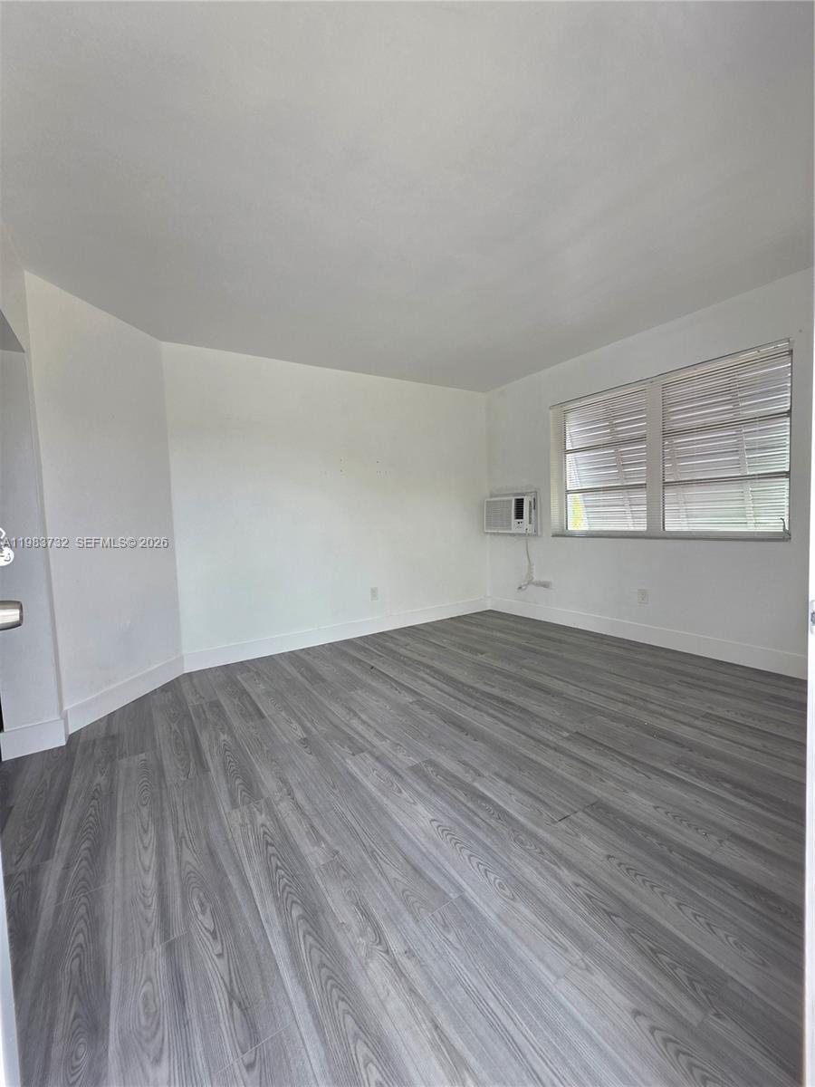 Vacant room with gray plank flooring, window blinds, and a wall-mounted air conditioner.