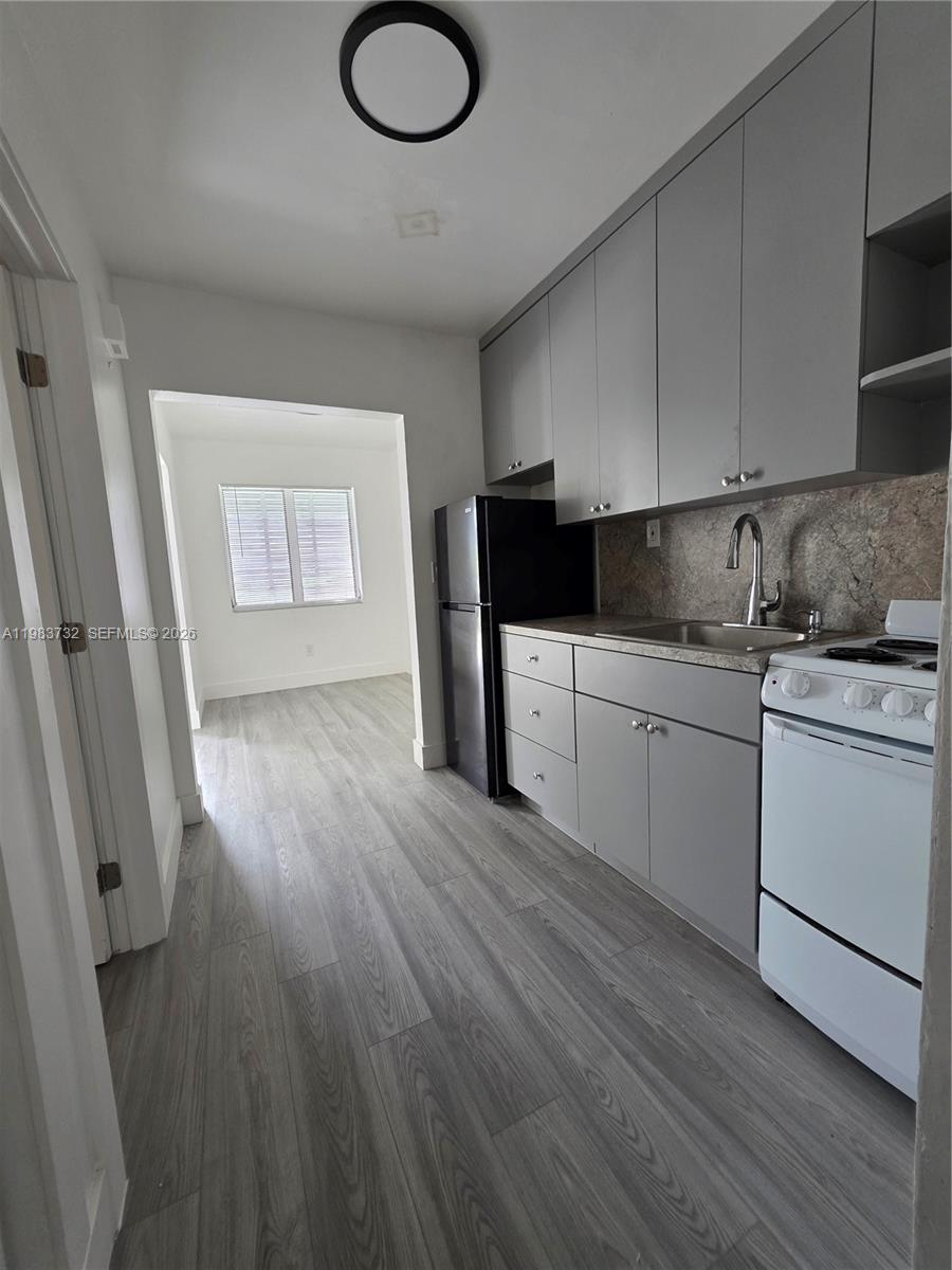 Unfurnished kitchen with gray cabinets, a stone-pattern backsplash, and gray wood-look flooring.