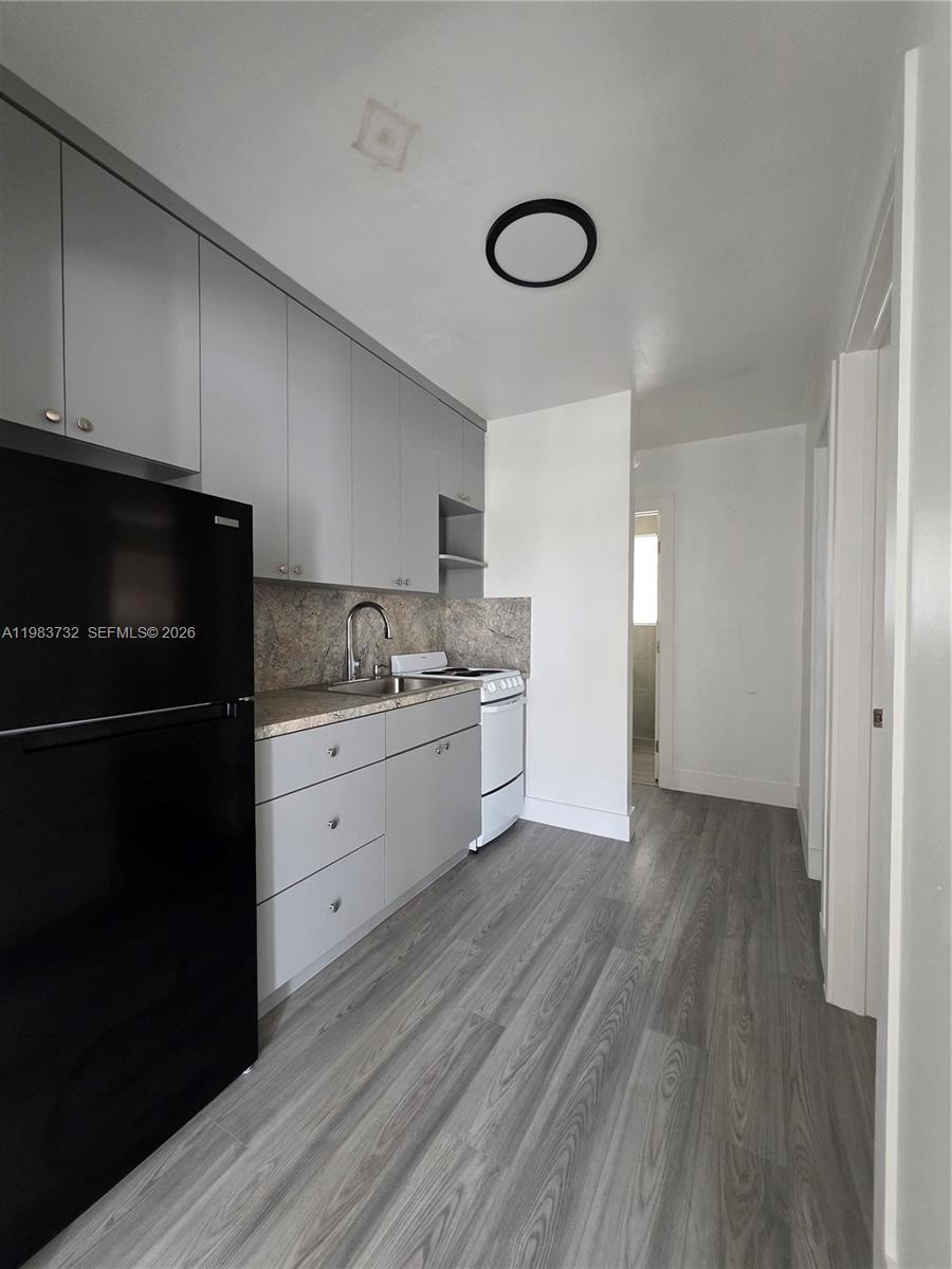 Vacant galley kitchen with gray cabinets, a black refrigerator, and gray wood-look flooring.