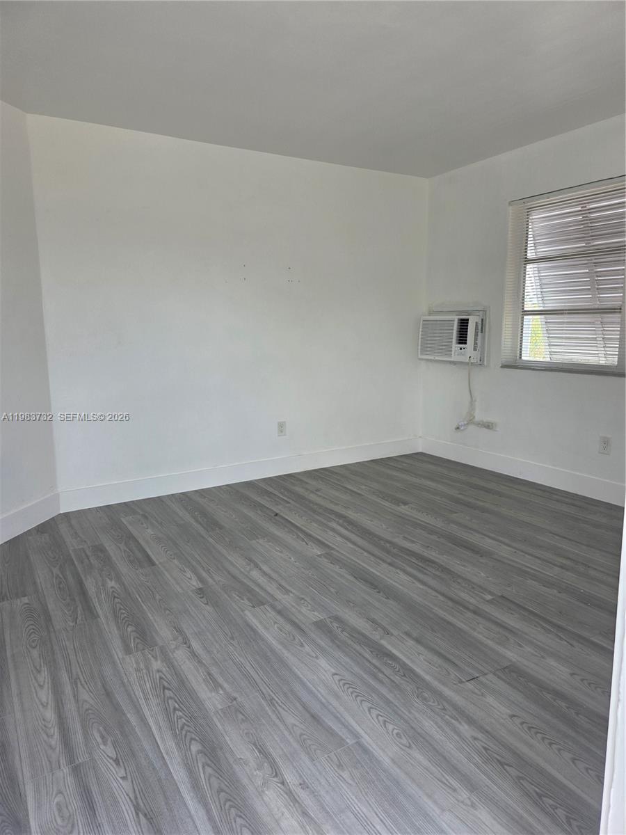 Empty room with gray plank flooring, window blinds, and a window air conditioner.