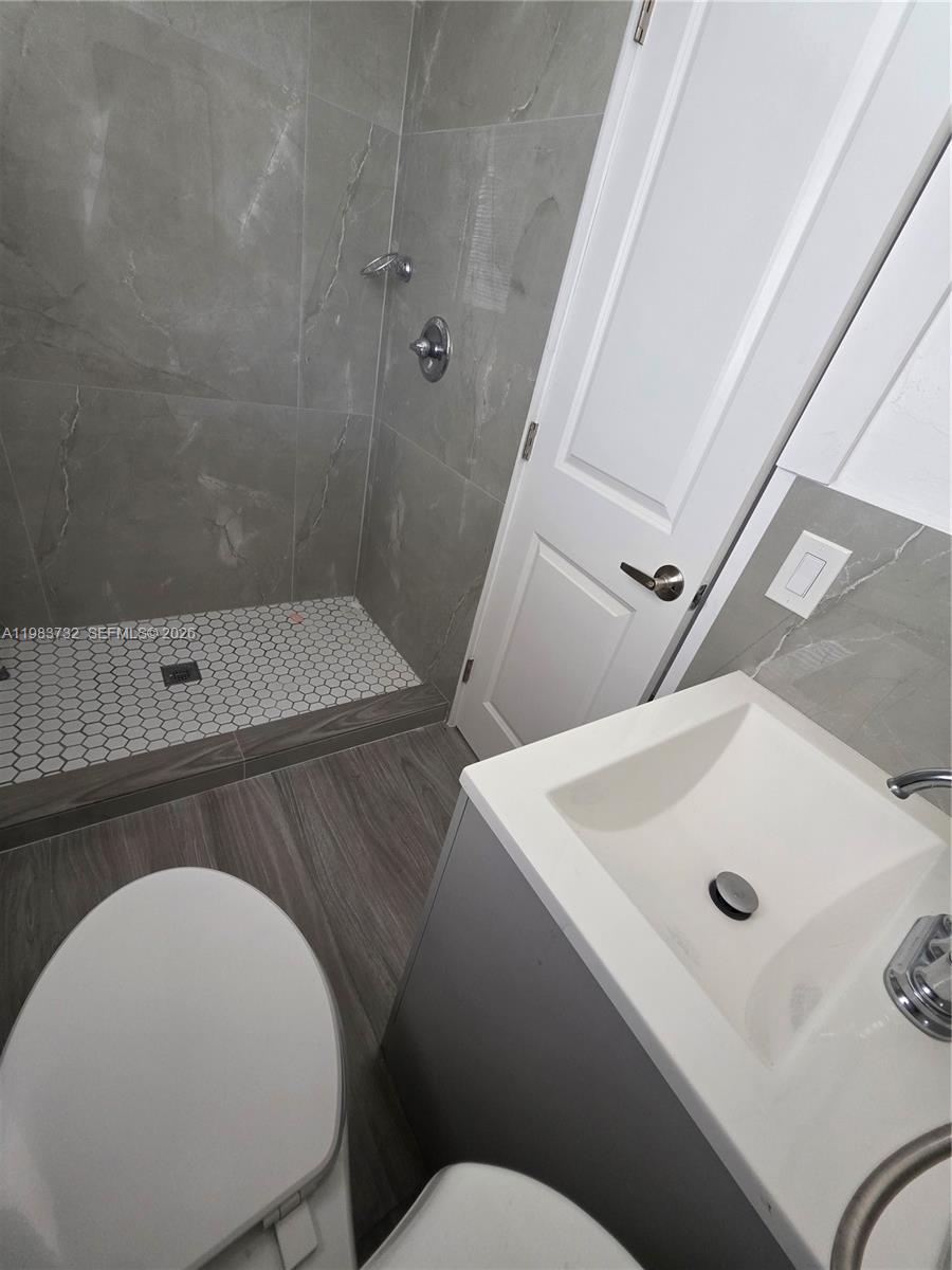 Bathroom with a gray tiled walk-in shower, white hexagonal shower floor, vanity sink, and toilet.