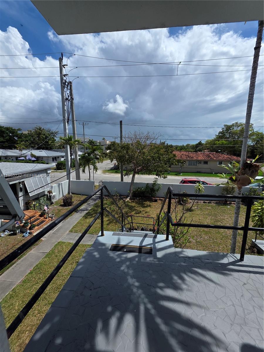 Raised tiled terrace with black railings overlooking a residential street and neighboring homes.
