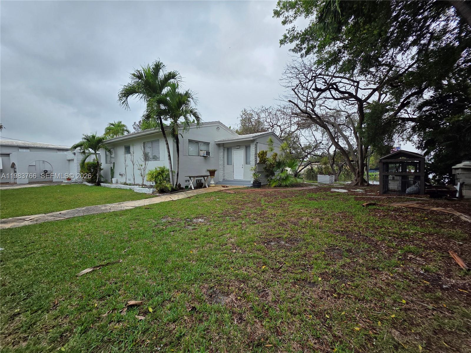 Single-story gray house with palm trees and a broad grassy front yard.