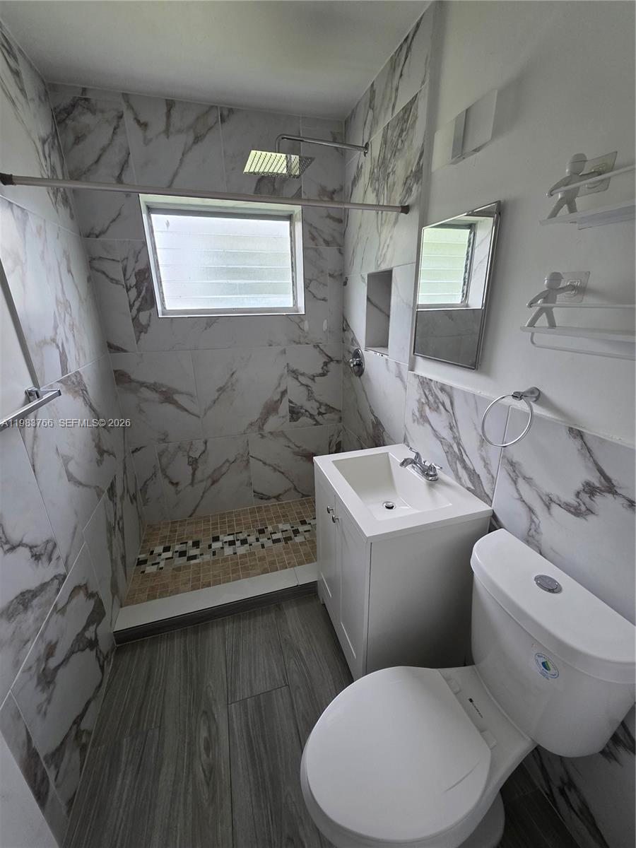 Bathroom with marble-look shower walls, a small window, and a white vanity and toilet.