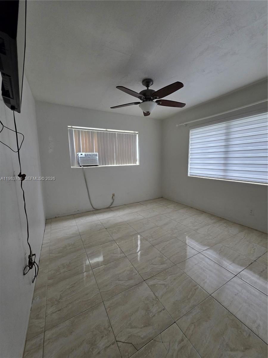 Empty tiled room with a ceiling fan, window air conditioner, and two shaded windows.