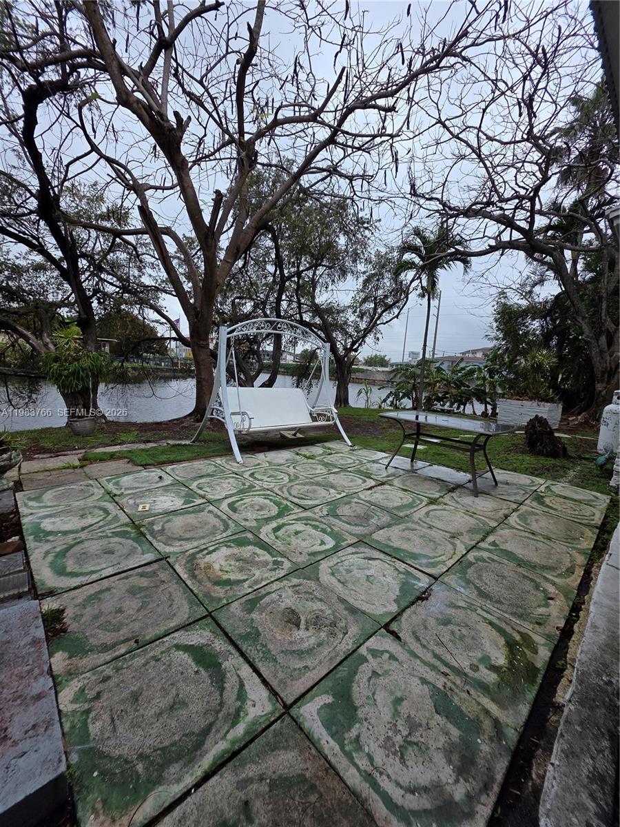 Stone patio with a white porch swing and table beside a tree-lined waterway.