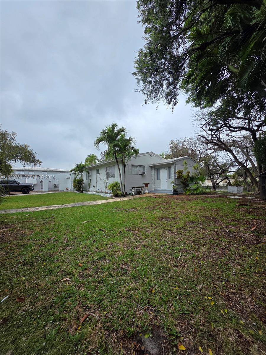 Single-story light-colored house with a covered entry, palms, and a broad grassy front yard.