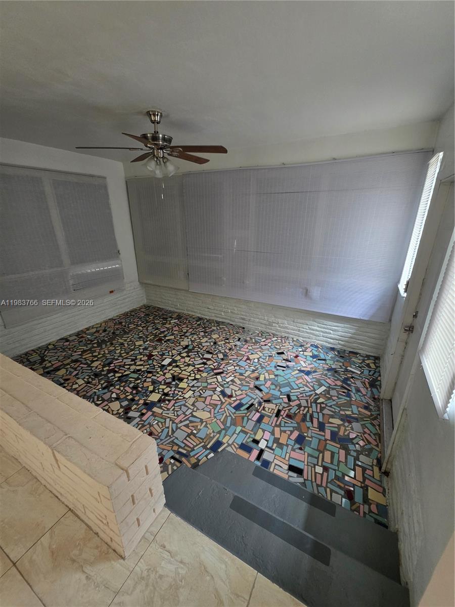 Empty sunroom with colorful mosaic tile flooring, covered windows, and a ceiling fan.