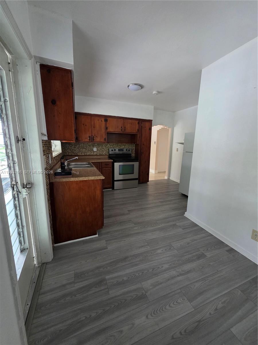 Unfurnished kitchen with dark wood cabinets, stainless-steel appliances, mosaic backsplash, and gray plank flooring.