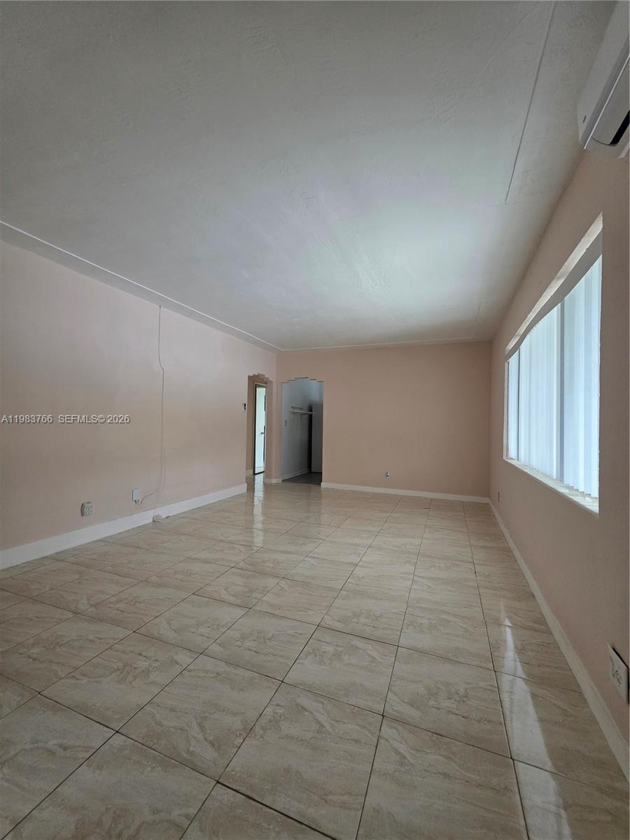 Empty room with glossy tiled floors, beige walls, and a wide window with vertical blinds.