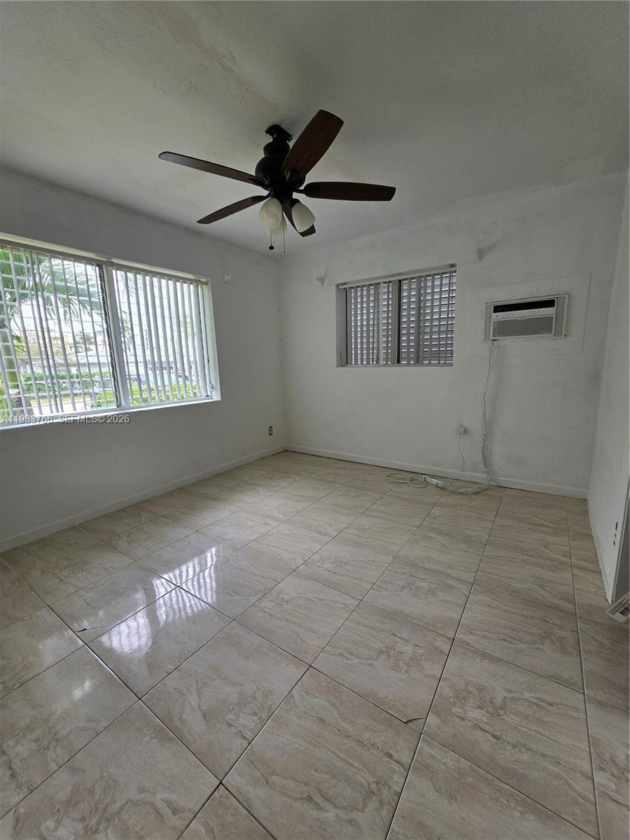 Vacant tiled room with a dark ceiling fan, two windows, and a wall-mounted air conditioner.