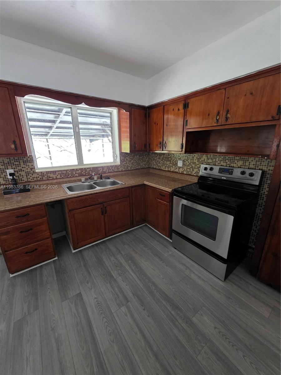 Kitchen with dark wood cabinets, mosaic tile backsplash, double sink, and stainless steel and black range.