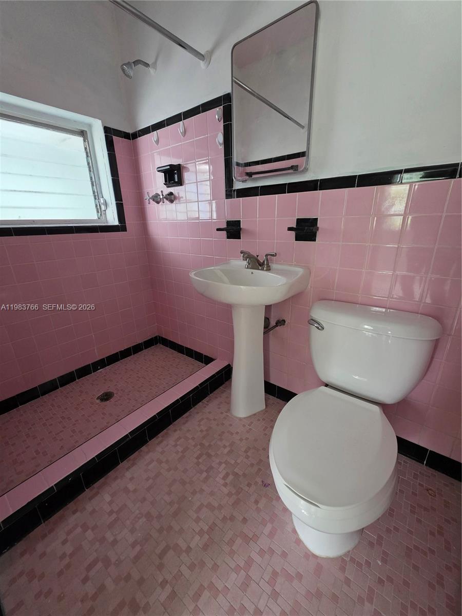 Bathroom with pink tile, black trim, a walk-in shower, pedestal sink, and toilet.