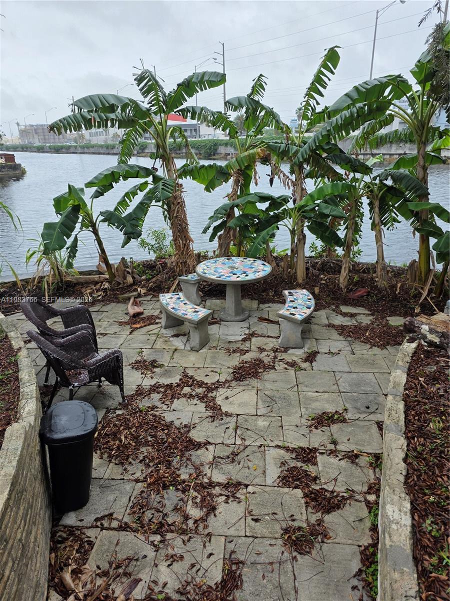 Waterfront patio with a mosaic table and benches, banana plants, and canal views.