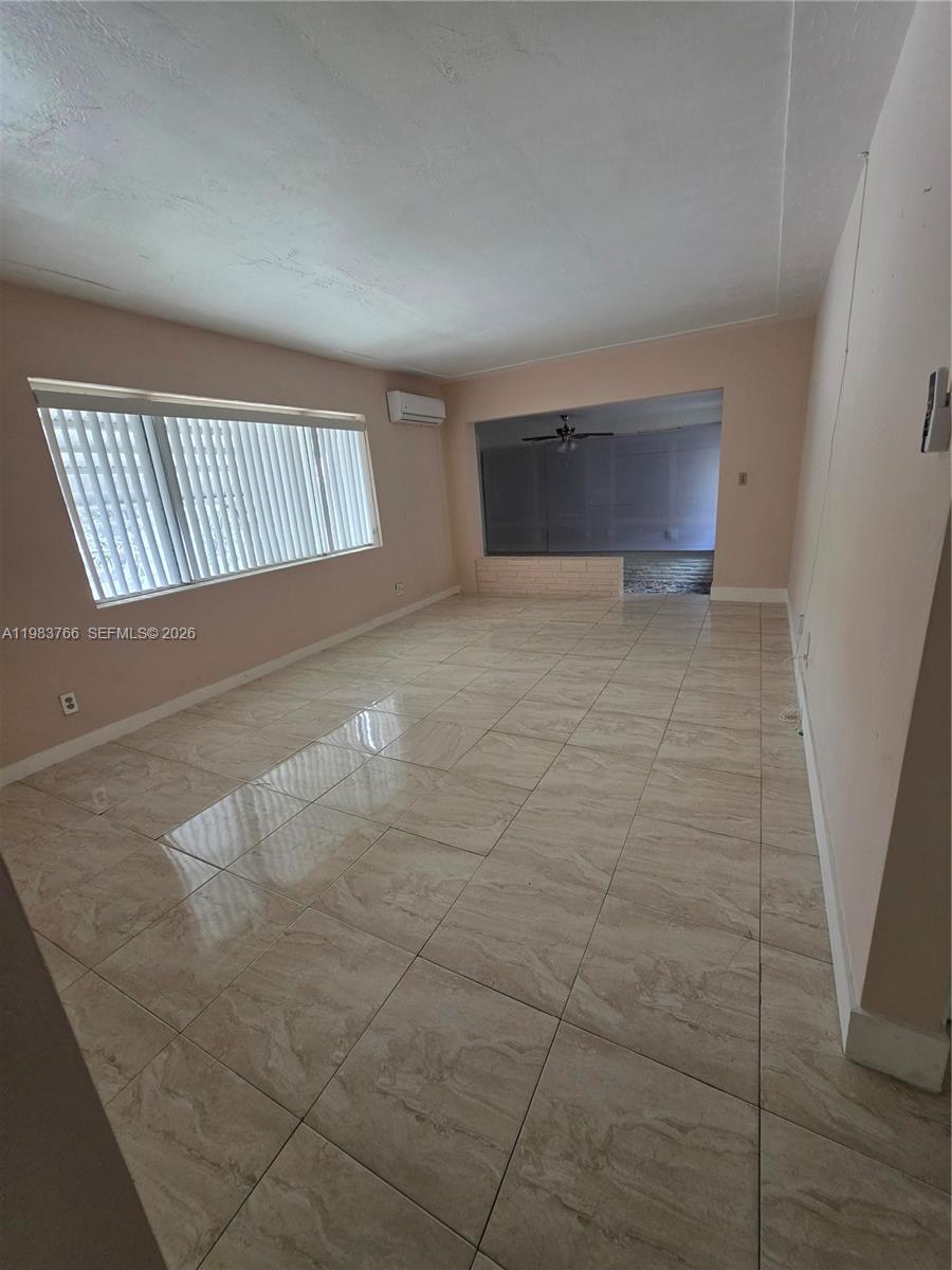 Unfurnished living room with glossy tile floors, vertical blinds, and a wall-mounted air conditioner.